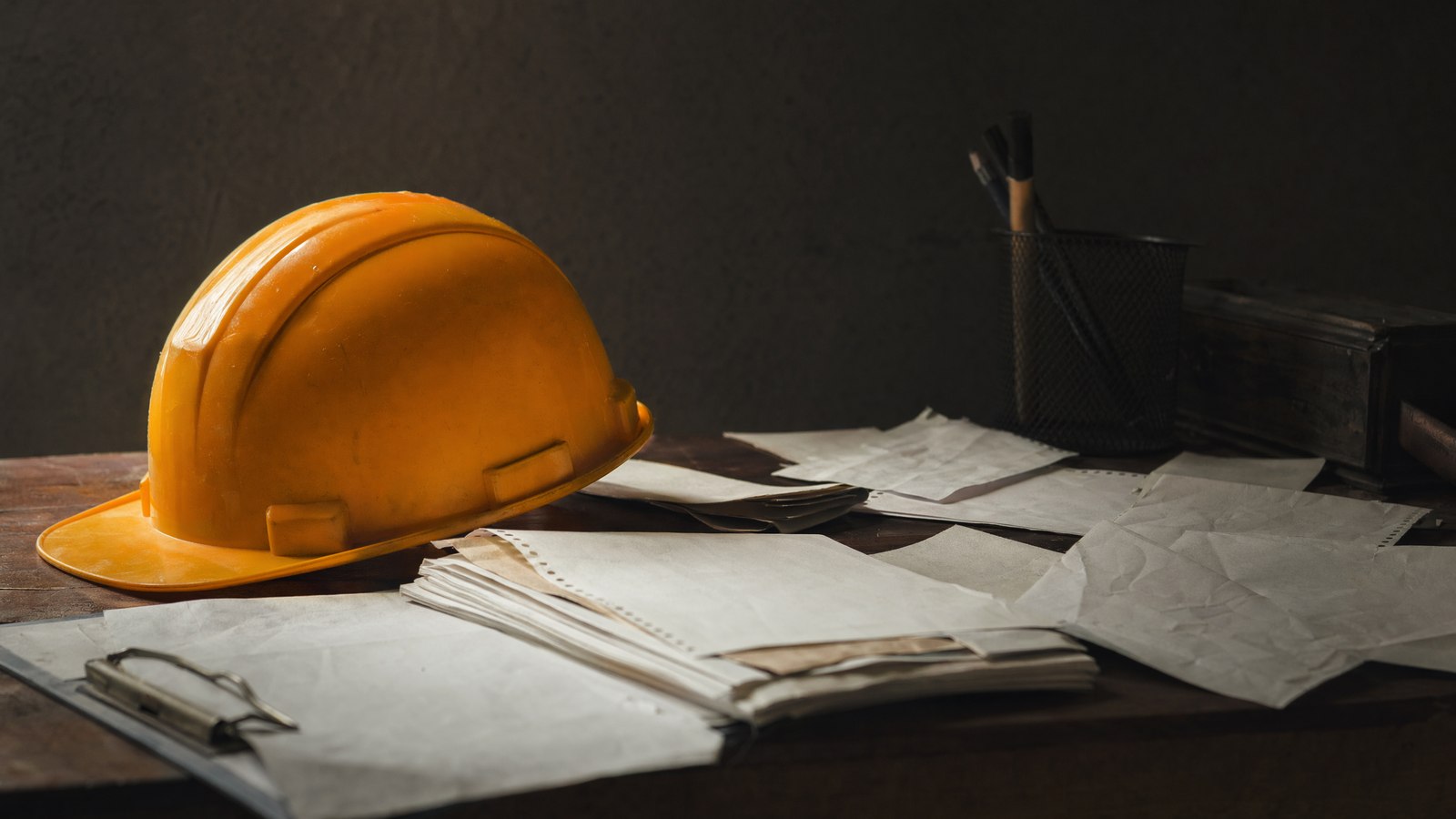 An amber hard hat resting on a desk surrounded by paper invoices